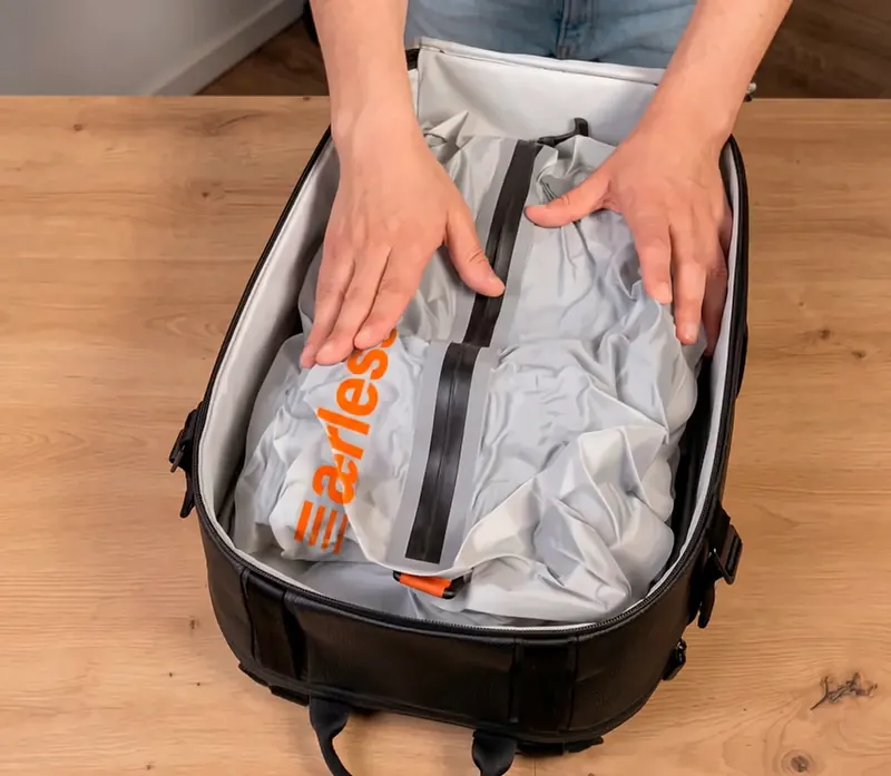 Hands pressing a flattened Aerless compression bag into a black travel backpack