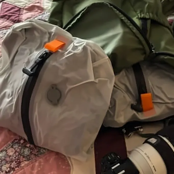 Compressed Aerless bag with orange zipper pull resting on a green hiking backpack