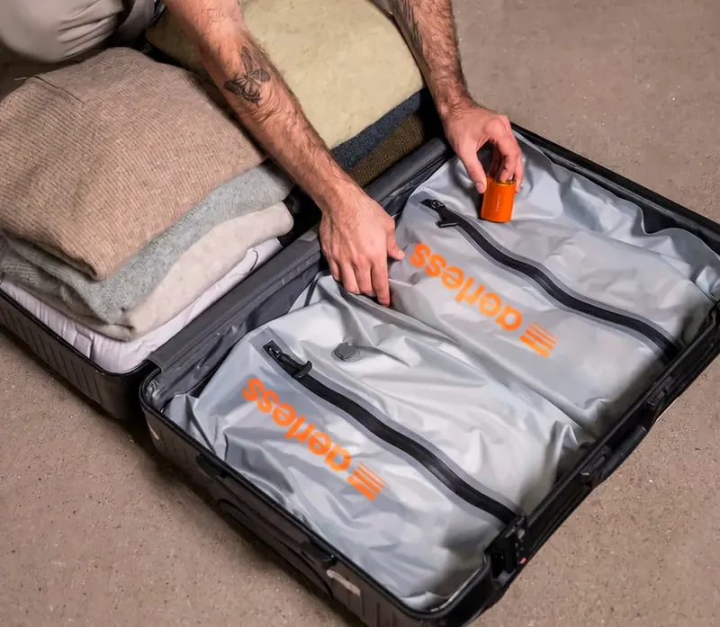 Traveler placing the orange Aerless pump on a filled bag inside an open suitcase next to folded sweaters