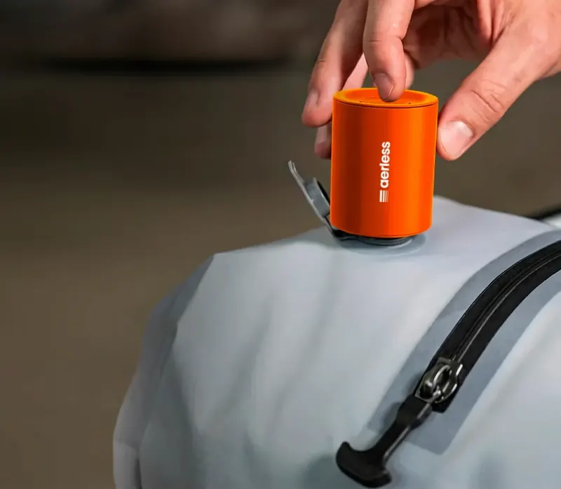 Hand pressing the compact orange Aerless USB-C pump onto the round valve of a grey vacuum bag